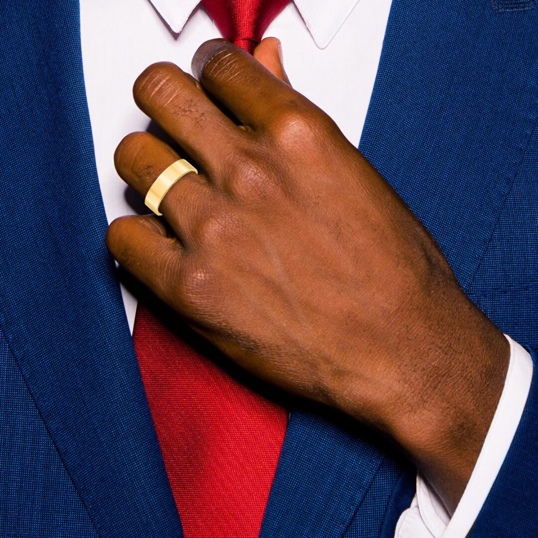 Man adjusting red tie, wearing blue suit and two gold rings.