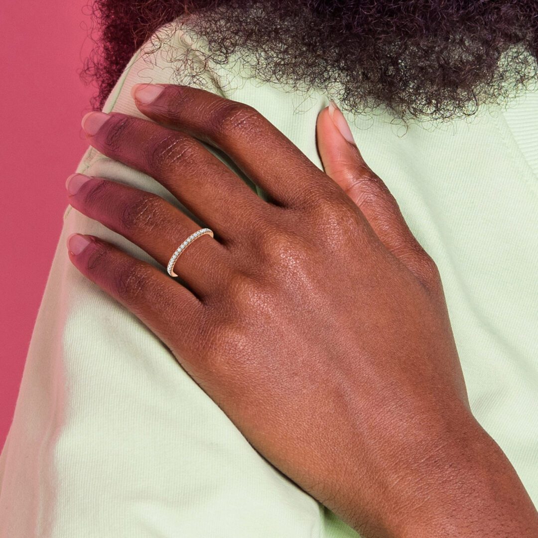 Hand with a gold ring resting on white fabric against a pink background.