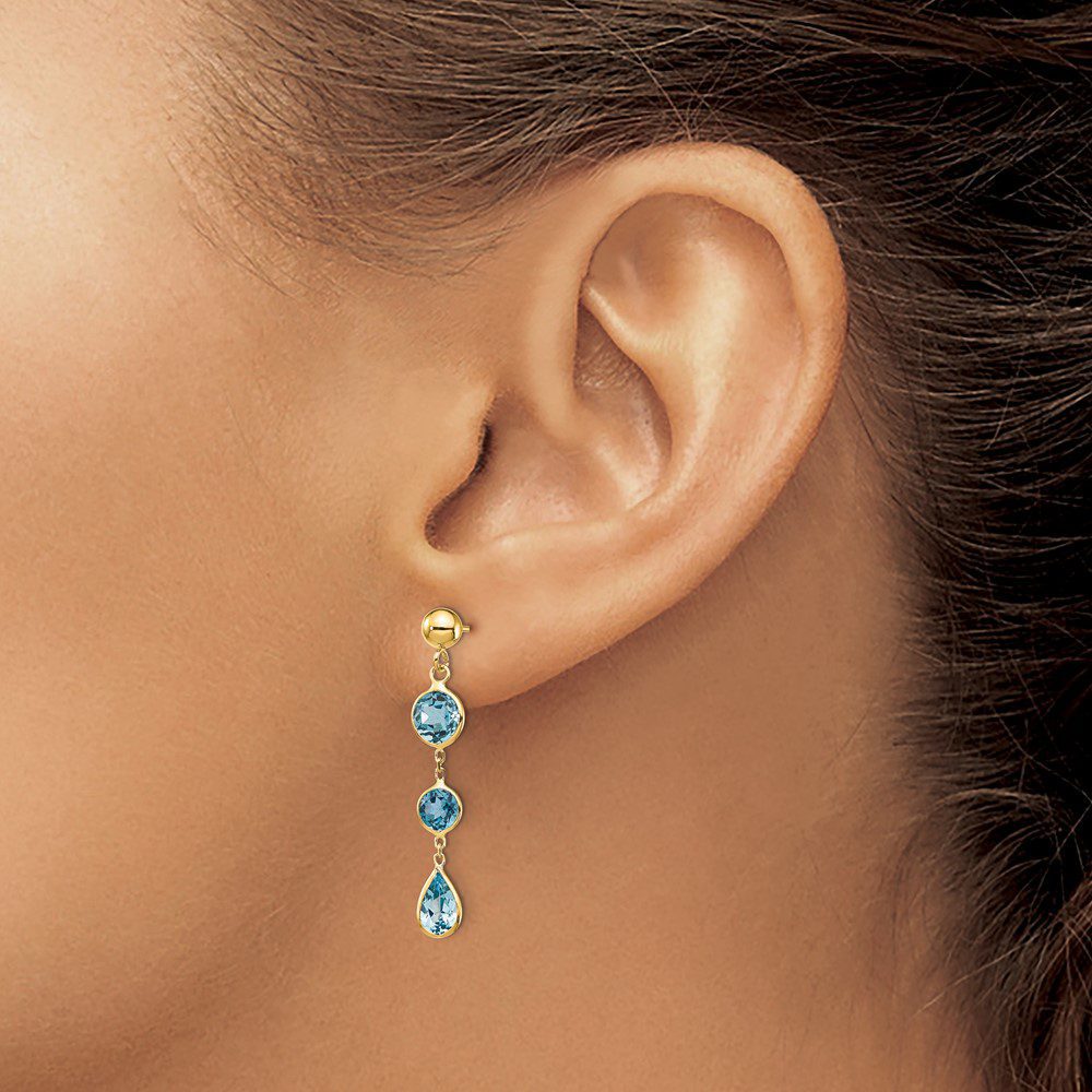 Elegant gold earring with blue gemstones on a woman's ear.